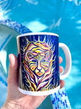 Load image into Gallery viewer, Mug with an image of a tiger with flames around him. The mug is colorful and the background is a blue pool. A hand is holding the mug