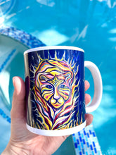 Load image into Gallery viewer, Mug with an image of a tiger with flames around him. The mug is colorful and the background is a blue pool. A hand is holding the mug
